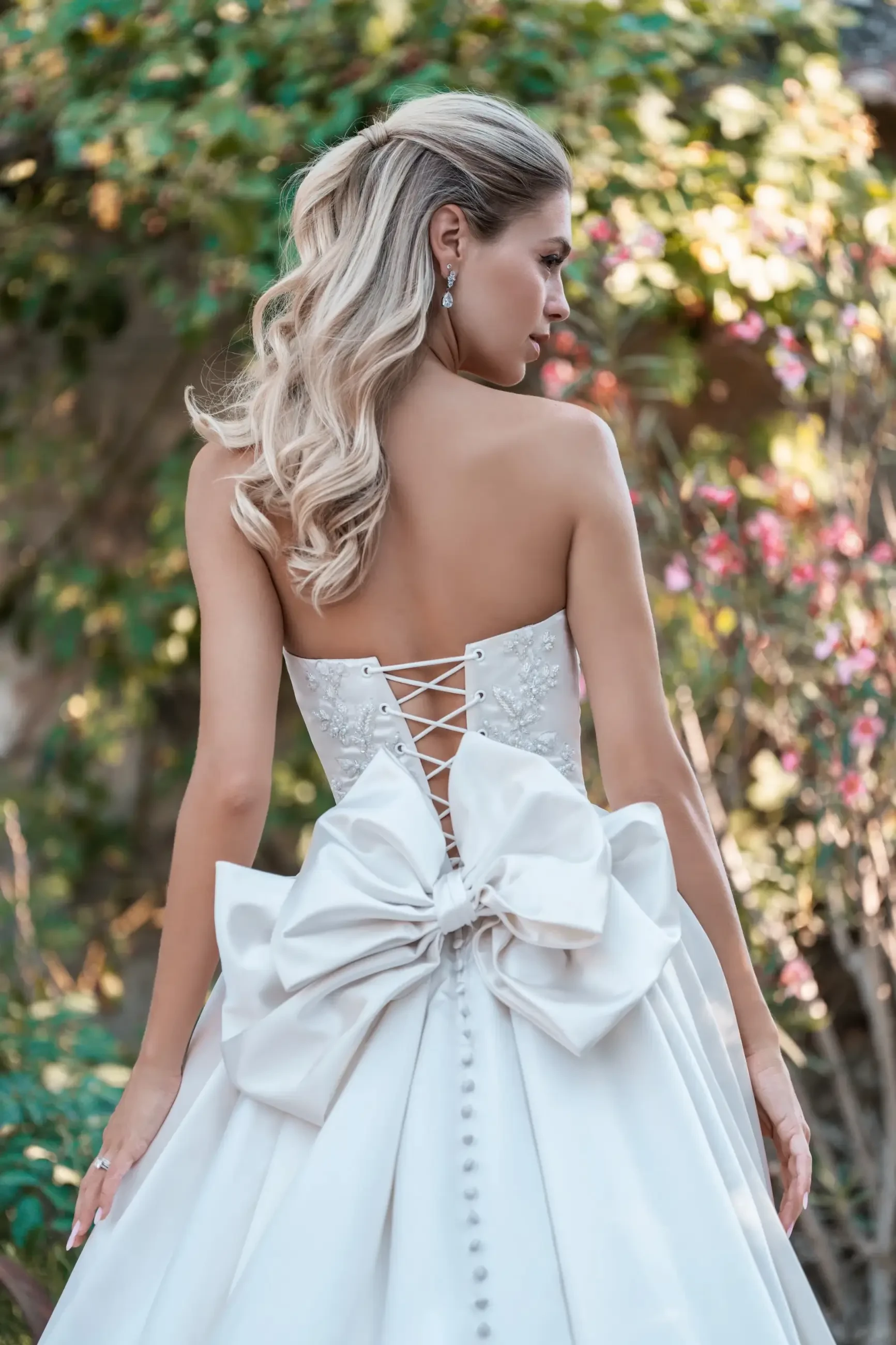 Model is wearing an off-the-shoulder satin ball gown with delicate beading and sequined appliques.