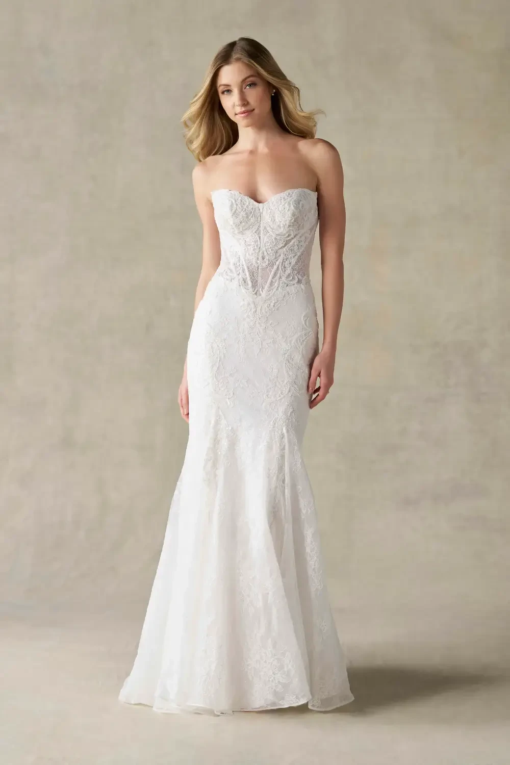 A model wearing a strapless, fitted white wedding gown with detailed lace embellishments.