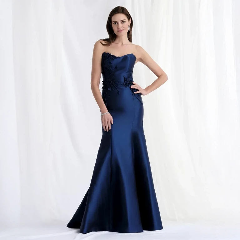 A bride in a white gown and veil smiles at a woman