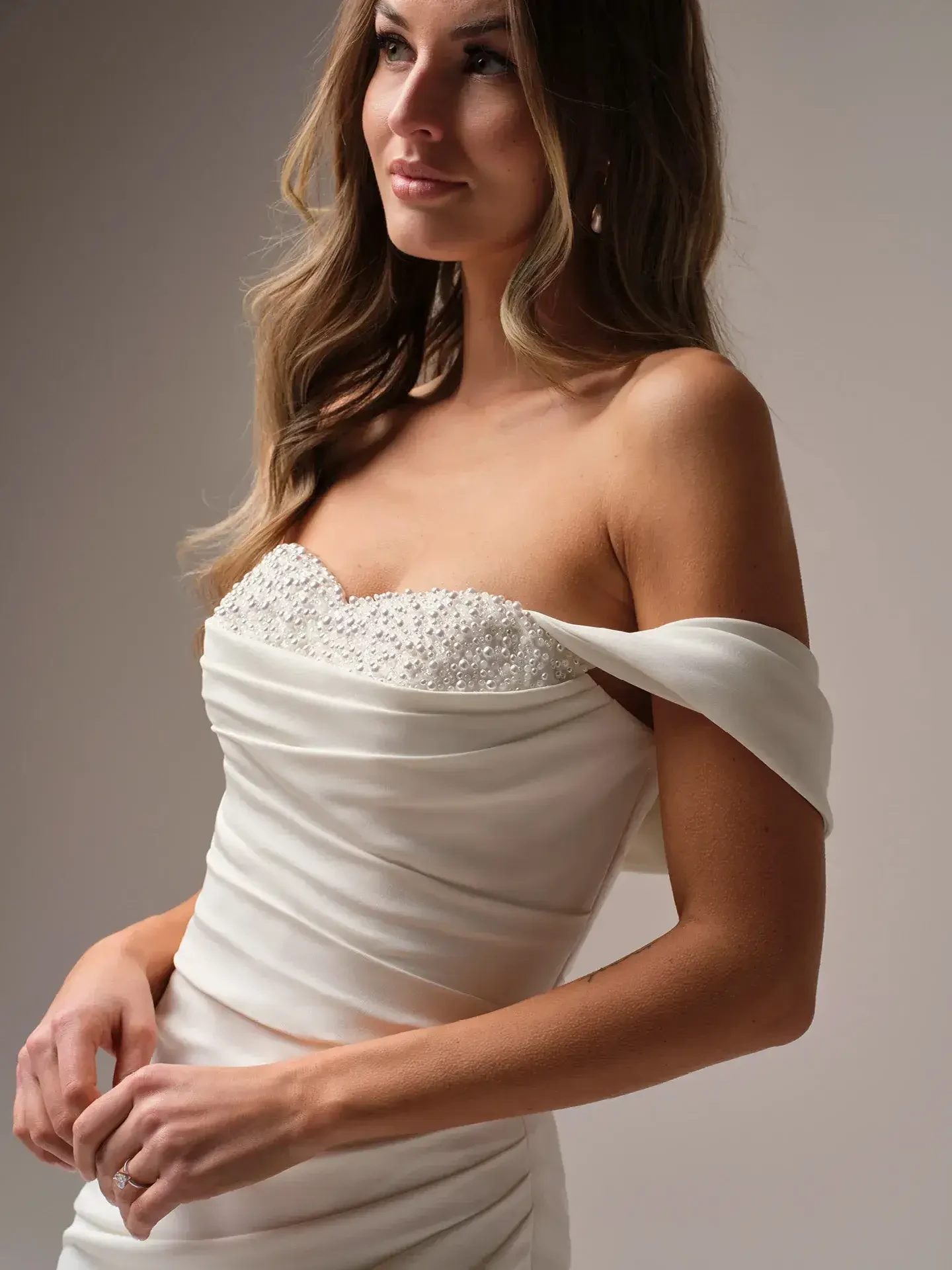 Model is wearing an off the shoulder wedding dress with beadwork peeking out under the bodice