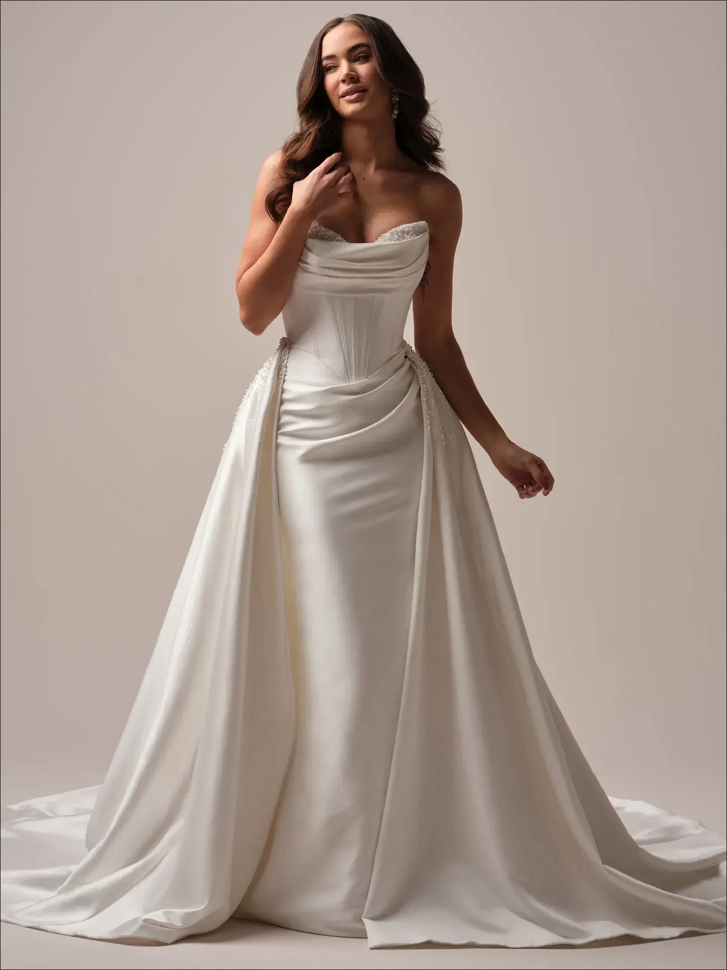 Model is wearing a structured pearl satin mermaid bridal dress with clean lines and a peekaboo detail at the bodice.